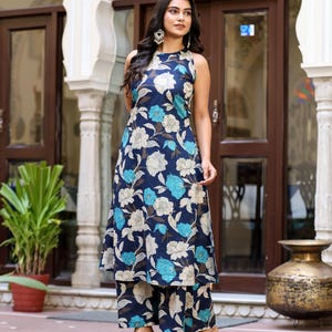 May include: A sleeveless navy blue floral print outfit, including a long tunic and matching wide-leg pants. The floral pattern features white, light blue, and brown flowers. The outfit is paired with gold heels.