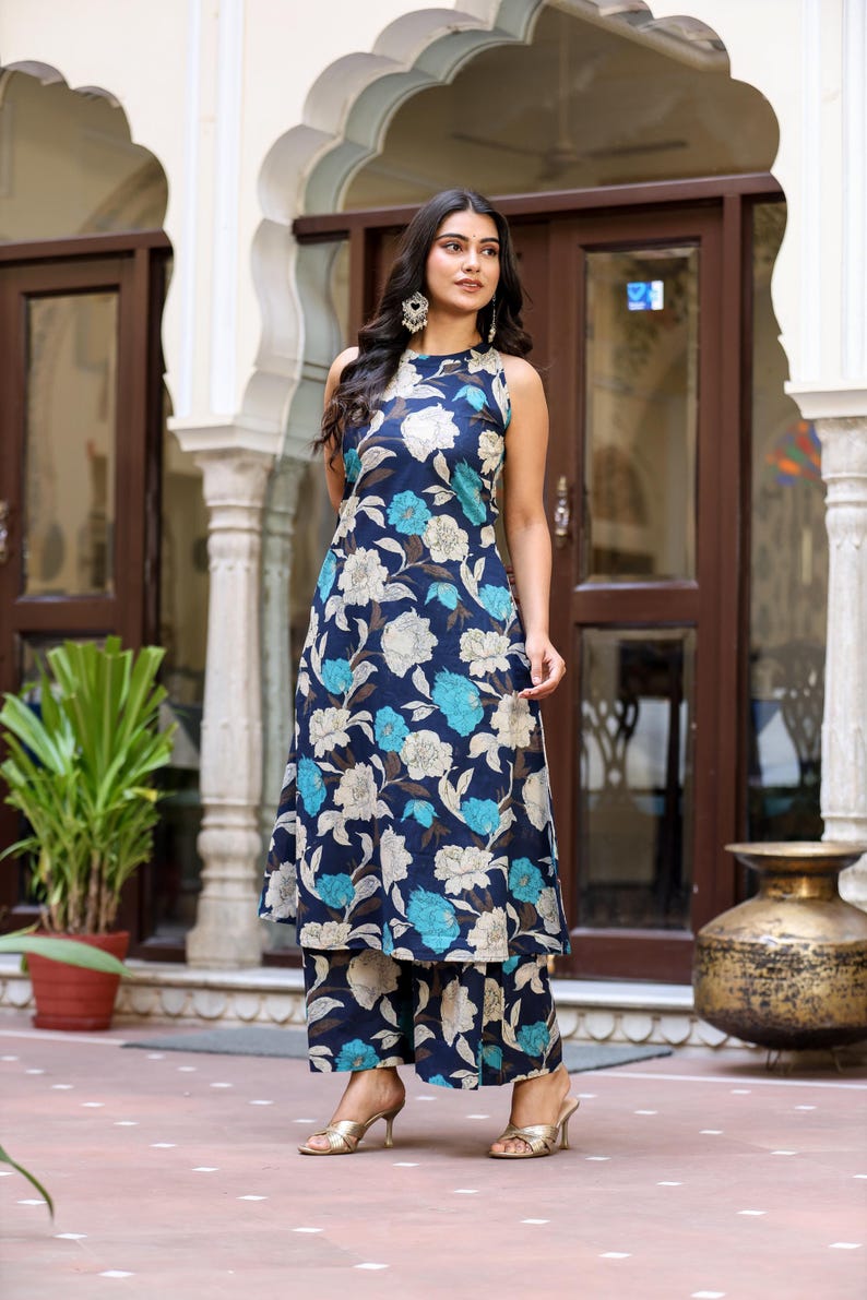 May include: A sleeveless navy blue floral print outfit, including a long tunic and matching wide-leg pants. The floral pattern features white, light blue, and brown flowers. The outfit is paired with gold heels.