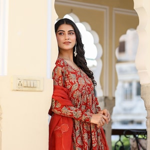 Puede incluir: Un vestido rojo con estampado floral con mangas largas y una bufanda roja a juego. El vestido presenta un cuello en V y una silueta fluida. El estampado floral incluye tonos de azul, verde y beige.