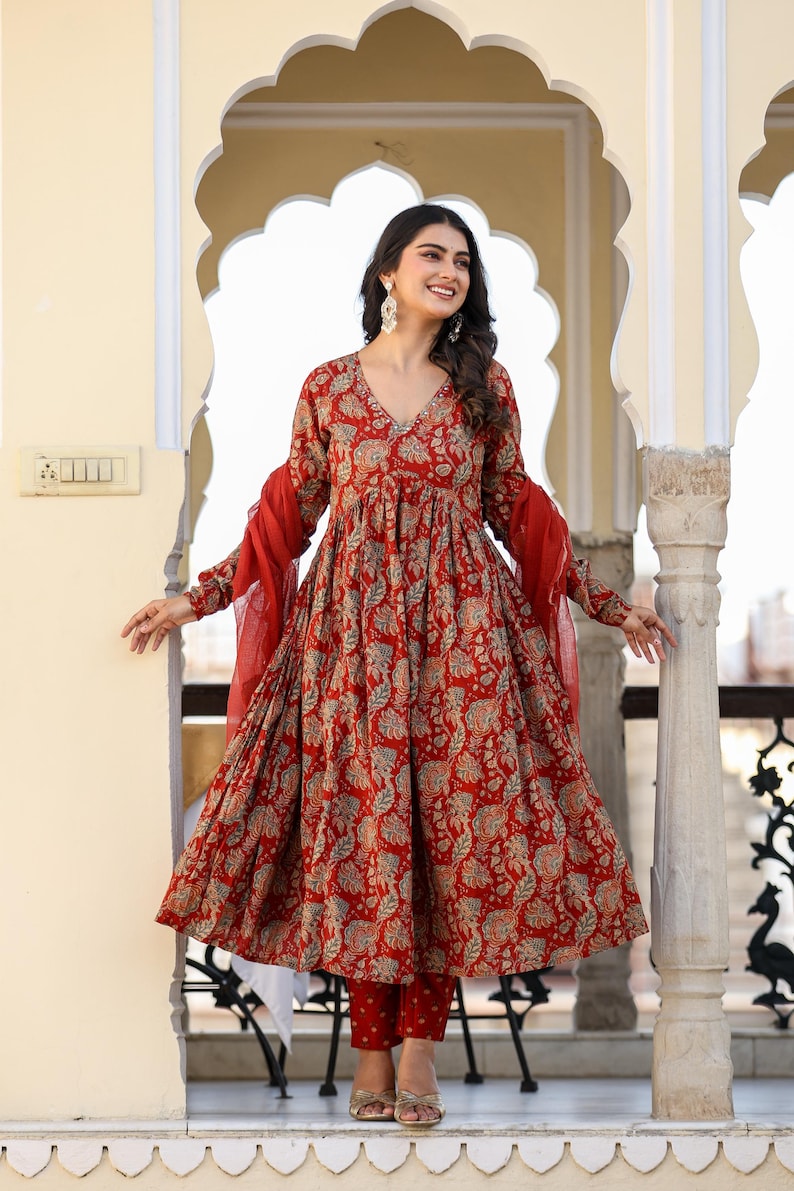 Puede incluir: Un vestido rojo con estampado floral con pantalones y bufanda a juego. El vestido tiene cuello en V y mangas largas. El conjunto est&aacute; hecho de una tela ligera y es adecuado para climas c&aacute;lidos. Es un estilo tradicional indio.