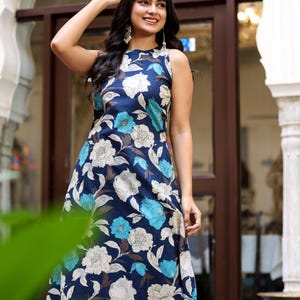 May include: Sleeveless navy blue floral print dress featuring white and turquoise flowers. The dress has a round neckline and a flowing silhouette, perfect for warm weather. The dress is made of a lightweight fabric.