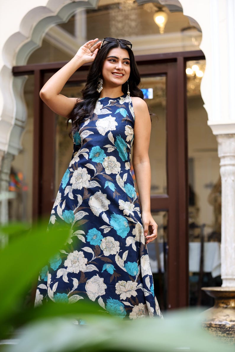 May include: Sleeveless navy blue floral print dress featuring white and turquoise flowers. The dress has a round neckline and a flowing silhouette, perfect for warm weather. The dress is made of a lightweight fabric.