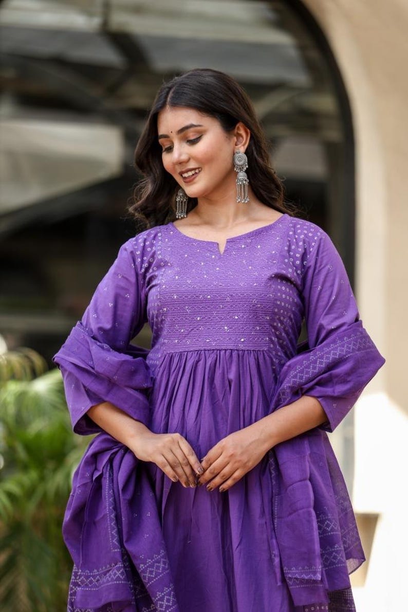 May include: A long, purple dress with a V-neck and long sleeves. The dress has detailed embroidery on the bodice and sleeves. A matching scarf is draped over the dress. The dress is made of a soft fabric.