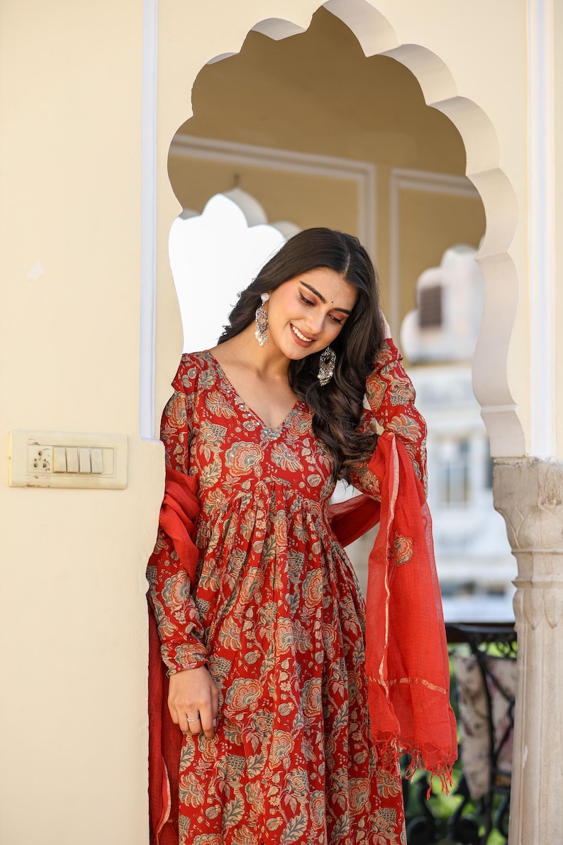 Puede incluir: Vestido rojo con estampado floral, mangas largas y cuello en V. El vestido se combina con una bufanda roja a juego. El vestido tiene una silueta fluida y un detallado estampado floral en tonos rojos, azules y beige.