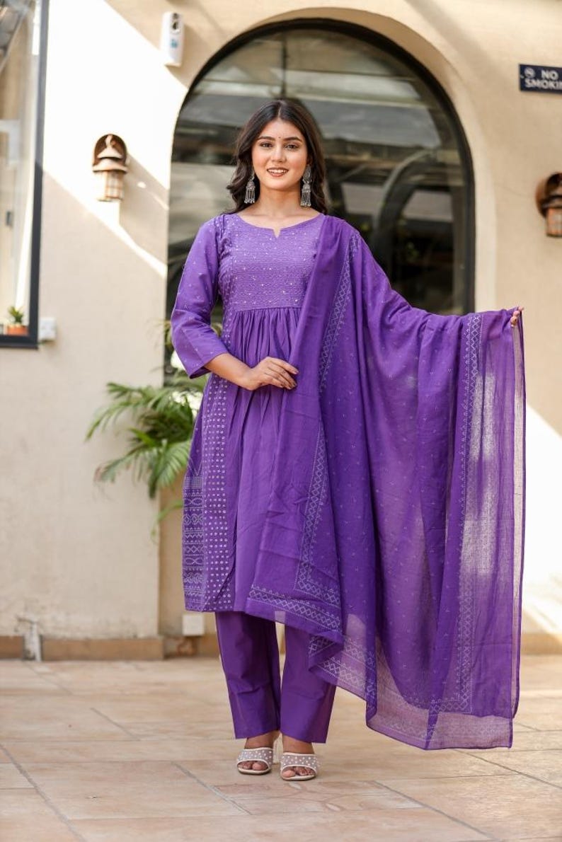 May include: A striking purple salwar kameez outfit. The set comprises a long-sleeved tunic with detailed embroidery, coordinated straight-leg trousers, and a flowing dupatta. The outfit is crafted from a lightweight material, ideal for warmer climates. The design features a delicate pattern.