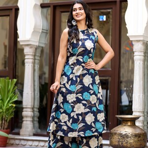 May include: A sleeveless, floral-print outfit in navy blue, light blue, and cream. The ensemble includes a top and matching wide-leg pants. The outfit is worn with gold heels. The background features architectural details.