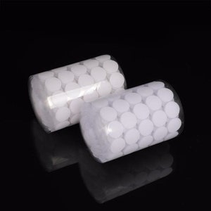 May include: Two rolls of white adhesive dots on a black background. The dots are arranged in a circular pattern on the rolls.