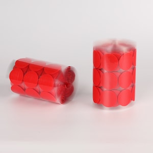 May include: Two rolls of red hook and loop fasteners, also known as sticky back dots, are shown on a white surface. The fasteners are in a clear plastic roll.
