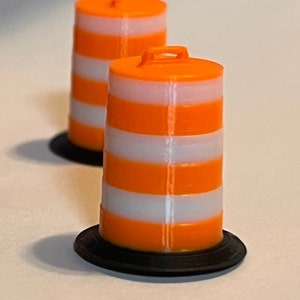Puede incluir: Dos pequeños conos de tráfico a rayas naranjas y blancas con bases negras. Cada cono tiene un asa en la parte superior. Los conos se utilizan para la construcción de carreteras y la seguridad.
