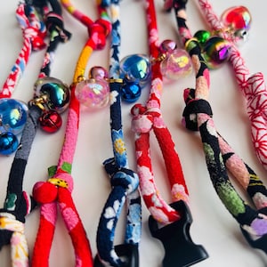 May include: Close-up of several colorful, patterned lanyards with decorative beads and black plastic clasps. The lanyards feature floral and geometric designs in red, pink, blue, and black, with iridescent and metallic beads.