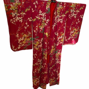 May include: A vibrant red kimono featuring an intricate all-over pattern of white cherry blossoms, yellow chrysanthemums, and green foliage. The garment has wide, long sleeves and a solid red inner lining, displayed hanging on a black hanger.