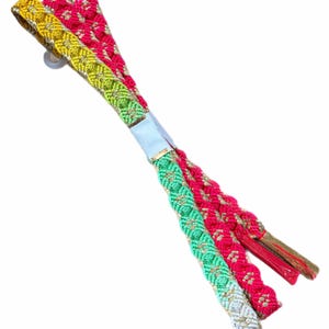 May include: A set of three braided fabric cords featuring a woven pattern in vibrant shades of hot pink, lime green, and mustard yellow, accented with metallic gold thread. The cords are secured together by a light blue paper band at the centre.