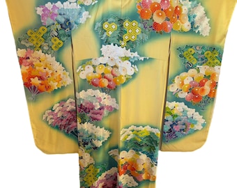 May include: A yellow kimono with a floral pattern. The kimono features a variety of colorful flowers, including orange, pink, white, and purple, set against a teal and yellow background. The garment is spread out, showcasing its full design.