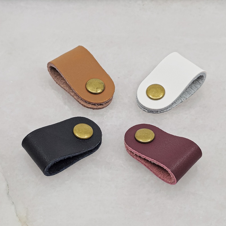 KALLACALLA leather cable organizer clips for charging cords and earphones, made with brass snap closure, shown in black, brown, white, and wine red. Cord management accessories for desk, travel, and everyday carry.
