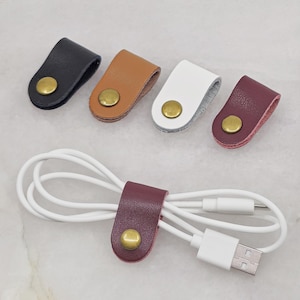 KALLACALLA leather cord organizer clip for chargers and headphones, shown in multiple color options with one in use.