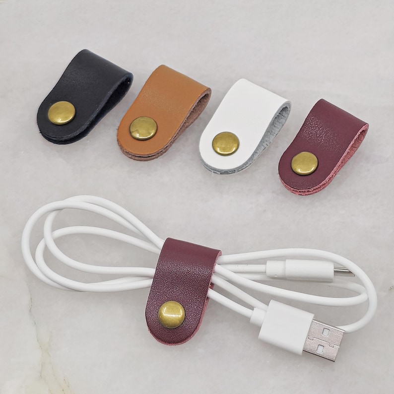 KALLACALLA leather cord organizer clip for chargers and headphones, shown in multiple color options with one in use.