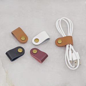 KALLACALLA leather cord organizer clips for phone chargers and earbuds, shown in assorted colors with one in use on a USB cable.