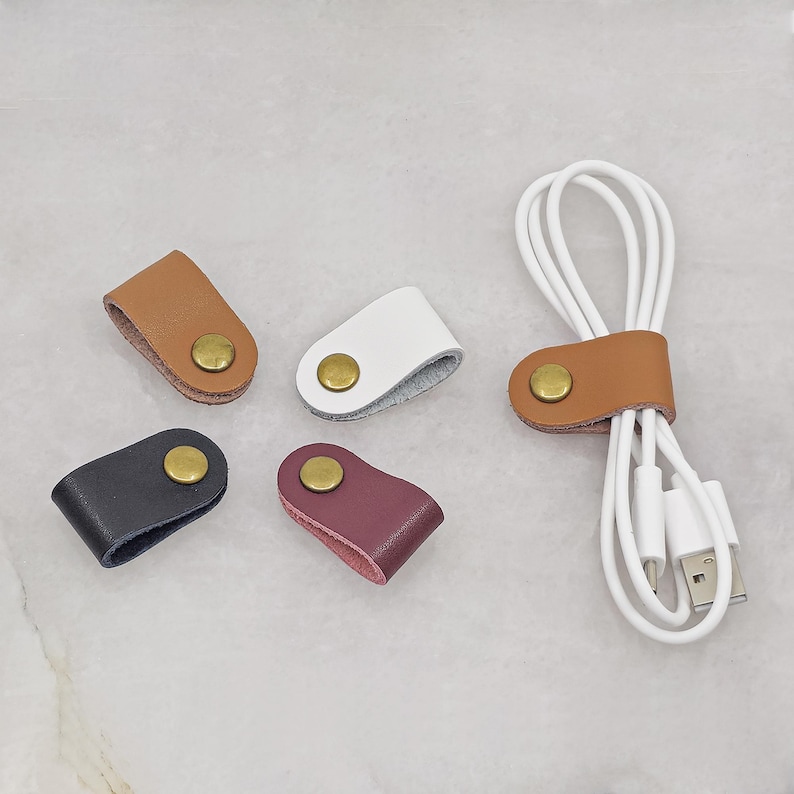 KALLACALLA leather cord organizer clips for phone chargers and earbuds, shown in assorted colors with one in use on a USB cable.