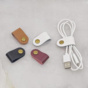 KALLACALLA leather cable organizer clips for chargers and earphones, shown in multiple colors with one in use.