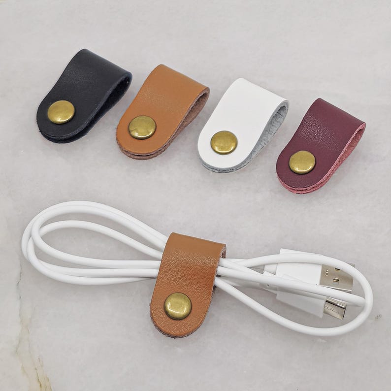 KALLACALLA leather cable organizer clips for phone chargers and tech cords, shown in multiple colors with one in use.