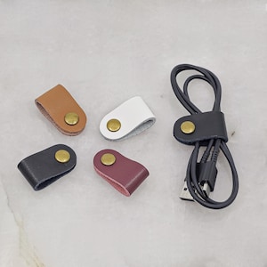 KALLACALLA leather cable organizer clips for chargers and earbuds, shown in assorted colors with one securing a black USB cord.