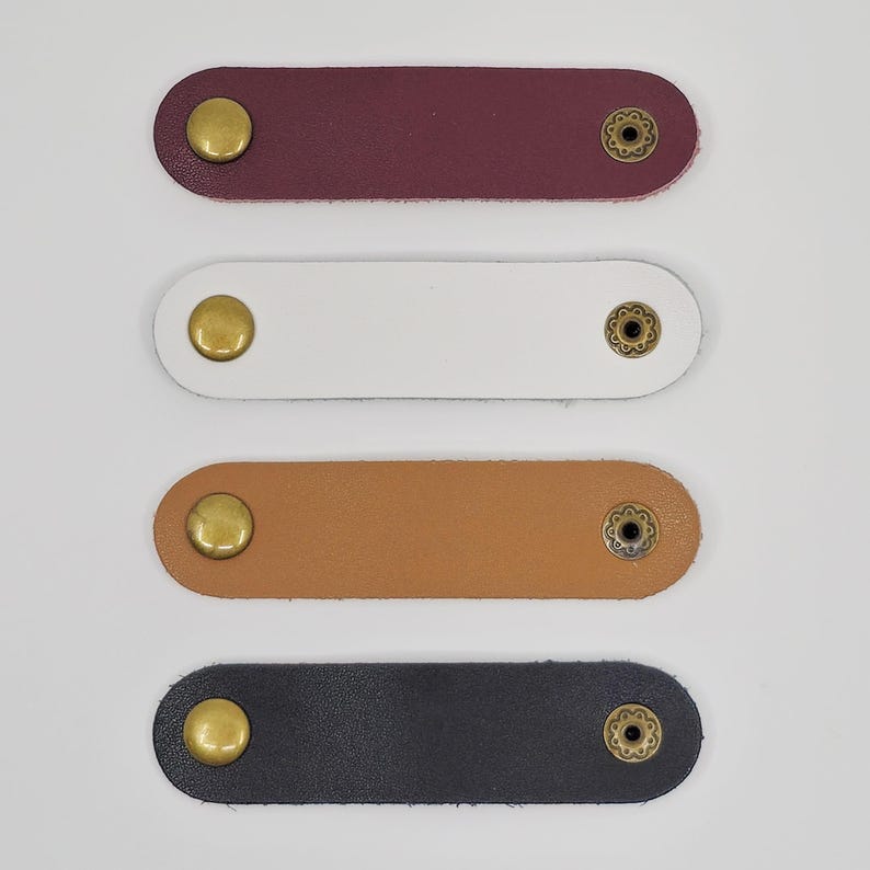 KALLACALLA leather snap cable organizer straps in multiple colors, used for phone chargers, tech accessories, and travel cord storage.