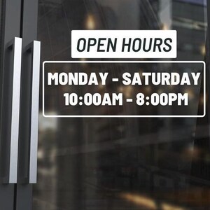 May include: Glass door with silver handles and a white sign that reads "OPEN HOURS". Below, a rectangular sign states "MONDAY - SATURDAY 10:00AM - 8:00PM". The door reflects the outside environment.