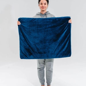 May include: A person holding a large, dark blue, rectangular cushion or pillow. The cushion is made of a soft, plush fabric.