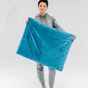 May include: A person holding a large, teal blue weighted blanket. The blanket is soft and plush, and it appears to be made of a high-quality material.