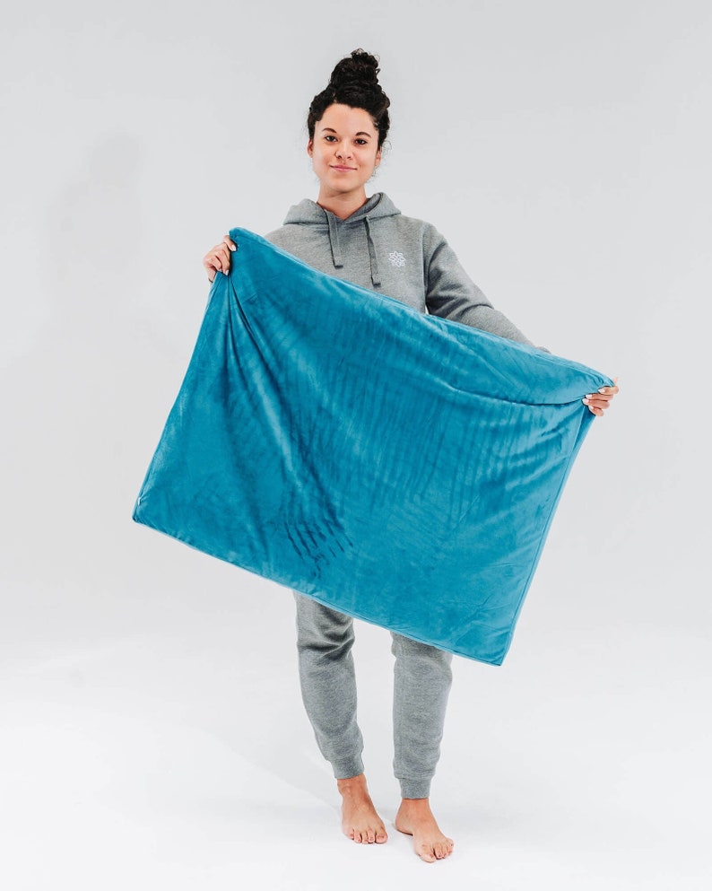May include: A person holding a large, teal blue weighted blanket. The blanket is soft and plush, and it appears to be made of a high-quality material.