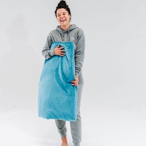 May include: A woman in a gray hoodie and matching sweatpants is holding a blue pillow. She is smiling and looking at the camera.