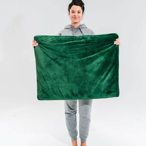 May include: A person is holding a green plush throw blanket in front of them. The blanket is soft and fluffy, and it would be perfect for cuddling up on the couch.
