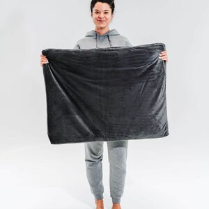 May include: A person is holding a dark gray weighted blanket in front of them. The blanket is soft and plush.