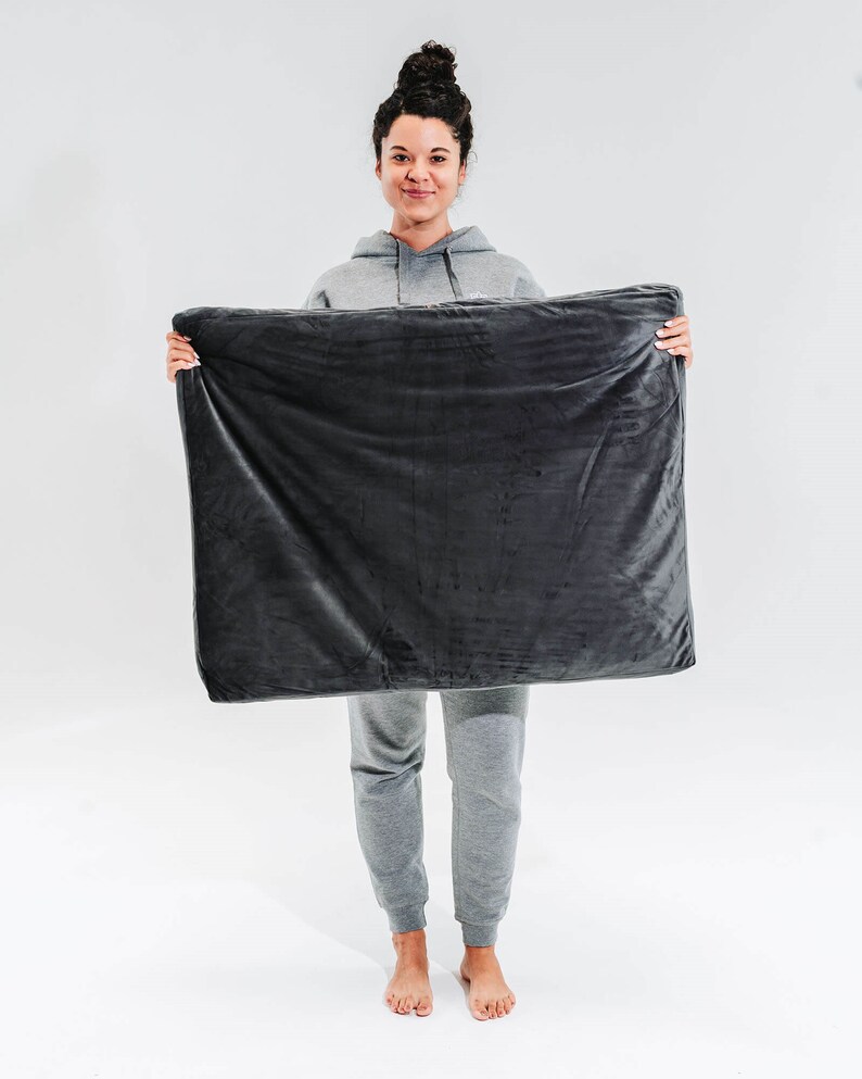 May include: A person is holding a dark gray weighted blanket in front of them. The blanket is soft and plush.