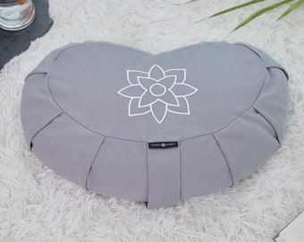 May include: Gray meditation cushion with a white embroidered lotus flower design. The cushion has a rounded shape and is filled with buckwheat hulls.