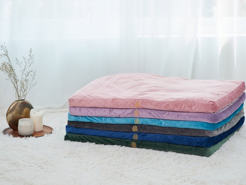 May include: A stack of six meditation cushions in various colors, including pink, purple, blue, gray, and green. The cushions are made of soft, plush velvet and are perfect for sitting or lying down on.