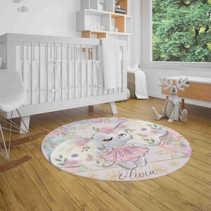 May include: A round pink and purple nursery rug with a floral design and a gray elephant wearing a pink tutu. The rug has the name "Olivia" written in gold glitter.
