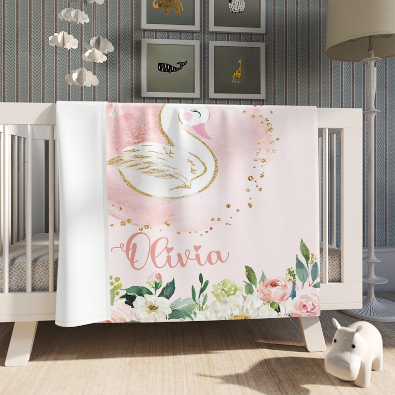 May include: Pink and white baby blanket with a gold glitter swan, floral accents, and the name "Olivia" written in pink.
