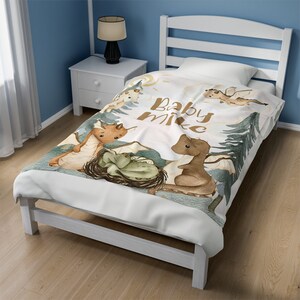 May include: A white baby blanket featuring a watercolour design of dragons and the text "Baby Mike". The blanket is on a white bed frame with a blue wall in the background.