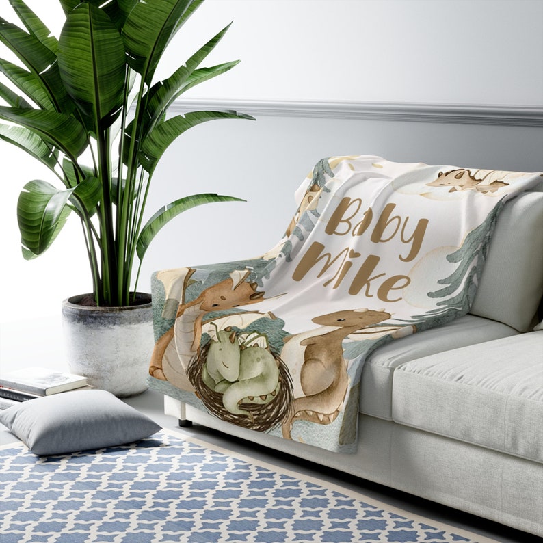 May include: A white baby blanket with a brown and green watercolour design of dragons and the text "Baby Mike".