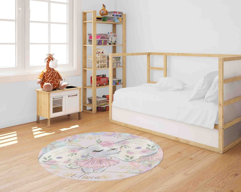 May include: A round pink and white rug with a floral design and a cartoon elephant wearing a pink tutu. The rug has the name "Olivia" written on it.