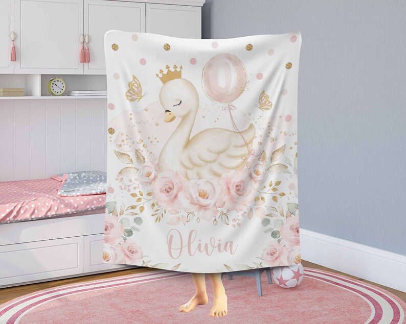 May include: A white and gold swan with a pink crown and a pink balloon is surrounded by pink and gold flowers. The text "Olivia" is written below the swan. The background is white with pink and gold polka dots.