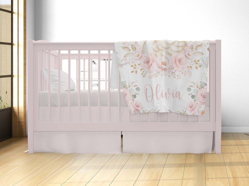 May include: A pink crib with a white crib sheet and a floral patterned baby blanket with the name "Olivia" on it.