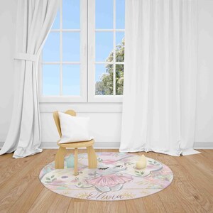 May include: A round pink and gold rug with a floral design and a cartoon bunny wearing a pink tutu. The rug has the name "Olivia" written in cursive on it.