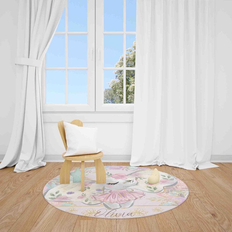 May include: A round pink and gold rug with a floral design and a cartoon bunny wearing a pink tutu. The rug has the name "Olivia" written in cursive on it.