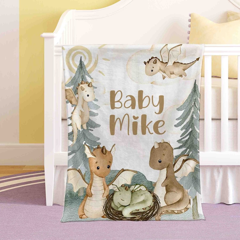 May include: A white baby blanket with a watercolour design of brown dragons and green trees. The text "Baby Mike" is written in brown letters on the blanket.