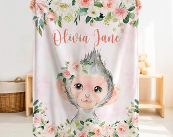 Könnte beinhalten: Eine rechteckige Decke mit einer Aquarellillustration eines Affen, der einen Blumenkranz trägt, umgeben von rosa und weißen Rosen sowie grünen Blättern. Der Name Olivia Jane ist in einer korallenfarbenen Schreibschrift aufgedruckt.