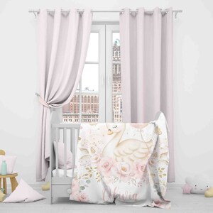 May include: A white crib with a pink and gold floral blanket featuring a swan with a balloon. The blanket has the name "Olivia" written on it.