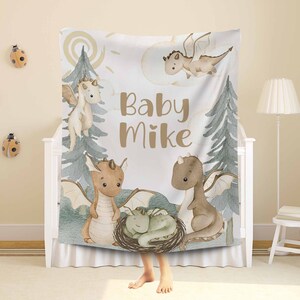May include: A white baby blanket featuring a watercolour design of dragons and trees. The blanket has the text "Baby Mike" in brown lettering.