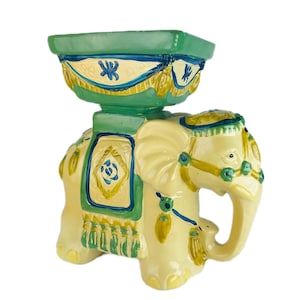 Könnte beinhalten: Ein Keramik-Elefanten-Pflanztopf mit einem grün-gelben bemalten Design. Der Elefant hält einen grünen Topf mit einem gelb-blauen bemalten Design.